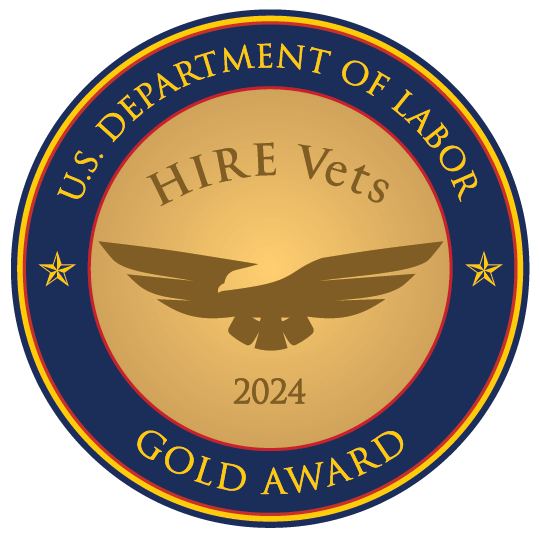 Gold outlined badge seal with the words U.S. Department of Labor Gold Award inside of a circular frame. In the middle, an image of the outline of a golden eagle with the words Hire Vets 2024